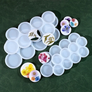 以下が含まれることがあります： レジン工芸用のシリコンモールド2セット。大きなセットは丸いモールドが12個、小さなセットは丸いモールドが10個。どちらも白で、ドライフラワーが飾られています。