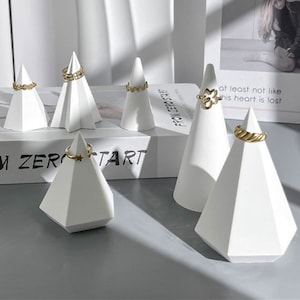 Può includere: Set di sei espositori per anelli geometrici bianchi. Gli espositori hanno la forma di piramidi e coni. Gli espositori sono perfetti per esporre anelli, orecchini o altri piccoli gioielli.