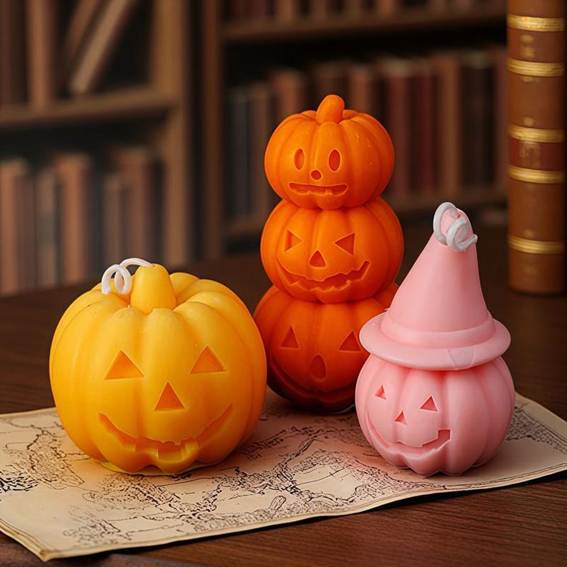 K&ouml;nnte beinhalten: Drei geschnitzte K&uuml;rbisdekorationen f&uuml;r Halloween. Einer ist gelb, einer rosa mit Hexenhut und der andere ist ein Stapel aus drei orangefarbenen K&uuml;rbissen. Alle haben geschnitzte Gesichter und sitzen auf einer Karte.