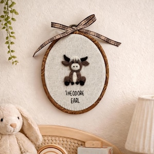 Peut inclure: D&eacute;coration murale ovale avec un cadre en bois marron et un motif de taureau en feutre. Le taureau est marron, blanc et noir. Le texte "THEODORE EARL" est en dessous. Un ruban &agrave; carreaux marron et beige est attach&eacute; en haut.