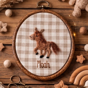 Peut inclure: Un cercle &agrave; broder en bois avec un cheval en feutre marron sur un tissu &agrave; carreaux beige et blanc. Le nom "Moah" est brod&eacute; en dessous du cheval. Le cercle est entour&eacute; d'&eacute;toiles en feutre et d'autres &eacute;l&eacute;ments d&eacute;coratifs.