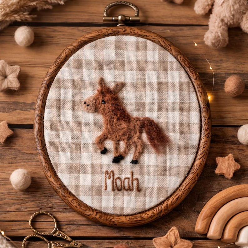 Peut inclure: Un cercle &agrave; broder en bois avec un cheval en feutre marron sur un tissu &agrave; carreaux beige et blanc. Le nom "Moah" est brod&eacute; en dessous du cheval. Le cercle est entour&eacute; d'&eacute;toiles en feutre et d'autres &eacute;l&eacute;ments d&eacute;coratifs.
