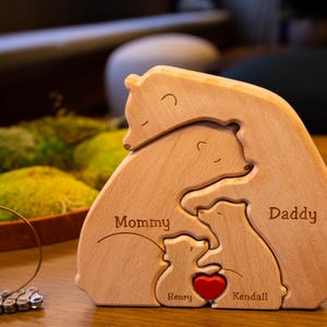 May include: Wooden bear family puzzle with the words "Mommy", "Daddy", "Henry", and "Kendall" engraved on the pieces. The bears are arranged in a hugging pose with a red heart in the center.