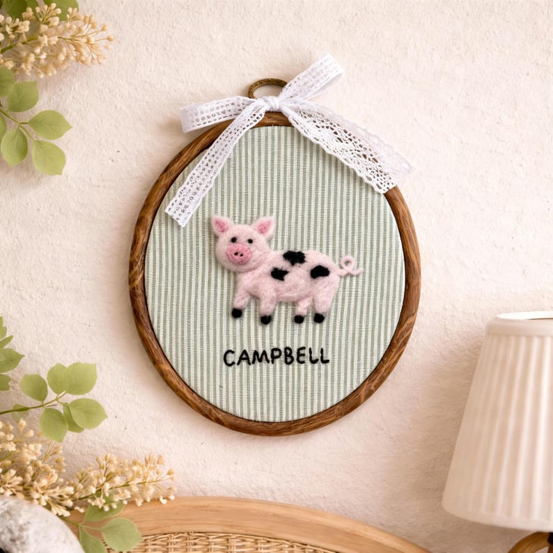 Peut inclure: D&eacute;coration murale circulaire avec un cadre en bois, repr&eacute;sentant un cochon rose avec des taches noires sur un fond &agrave; rayures vertes et blanches. Le nom "CAMPBELL" est imprim&eacute; en dessous du cochon. Un ruban de dentelle blanche est nou&eacute; en haut.