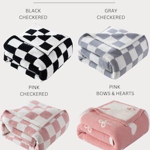 May include: Four folded throws, each measuring 50" x 70". The throws are in black and white checkered, gray and white checkered, pink and white checkered, and pink with bows and hearts designs. The text "50" X 70" THROWS" is at the top.