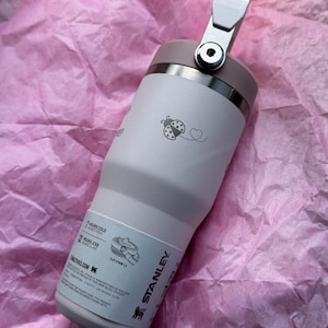 May include: A light pink Stanley tumbler with a flip straw and a handle. The tumbler has a ladybug and heart design. The tumbler is designed to keep drinks cold for 7 hours and iced for 12 hours.