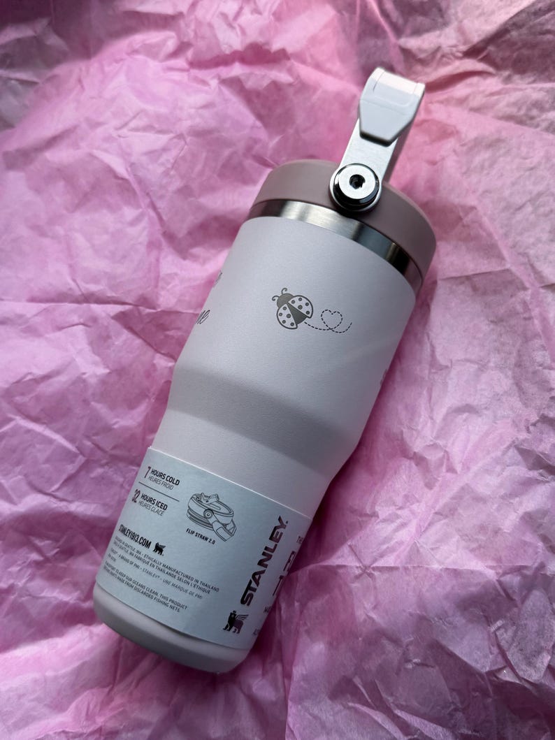 May include: A light pink Stanley tumbler with a flip straw and a handle. The tumbler has a ladybug and heart design. The tumbler is designed to keep drinks cold for 7 hours and iced for 12 hours.