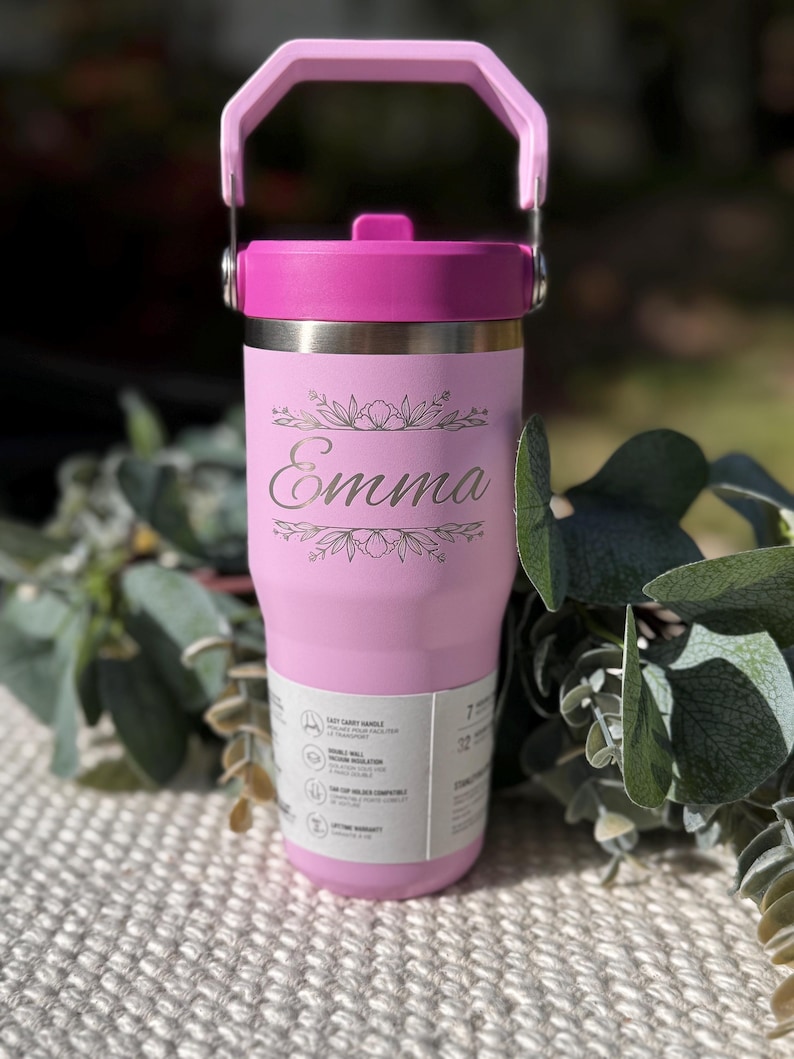 May include: A pink insulated tumbler with a matching handle and lid. The tumbler features the name "Emma" in a decorative font, surrounded by floral accents. The tumbler is designed to hold 32 ounces.