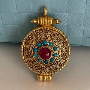May include: A gold-toned pendant with intricate floral designs and a red gemstone surrounded by turquoise stones.