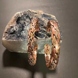May include: Two copper bracelets with a braided design. The bracelets are made of different shades of copper, creating a unique and textured look.