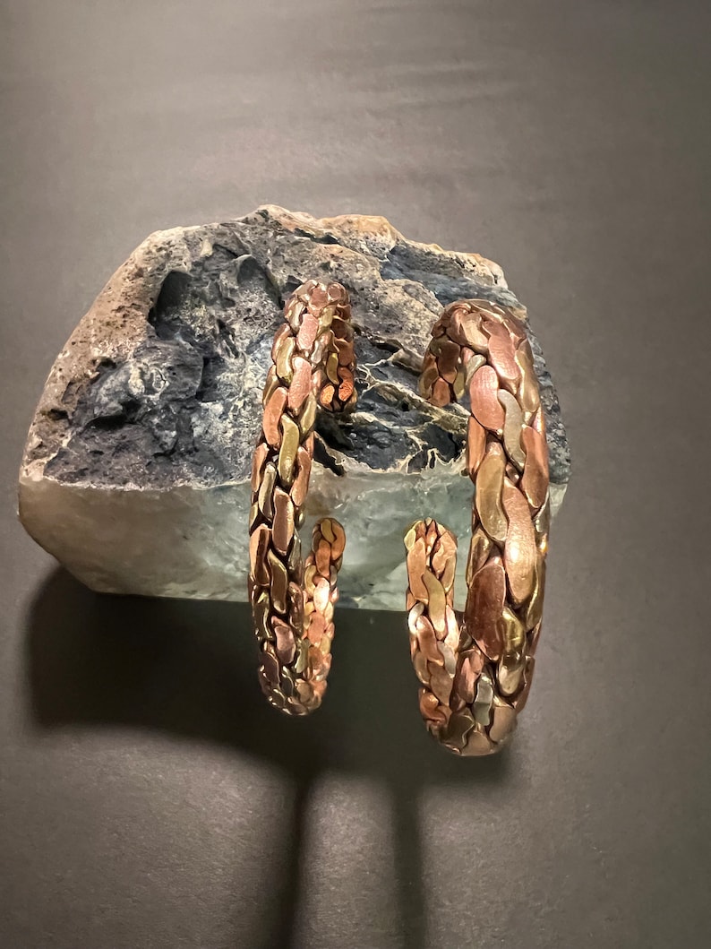 May include: Two copper bracelets with a braided design. The bracelets are made of different shades of copper, creating a unique and textured look.