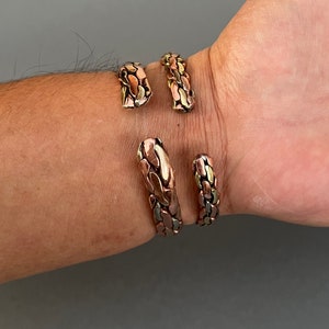 May include: Two copper bracelets with a textured, snake-like design. The bracelets are made of copper and have a gold and silver finish.