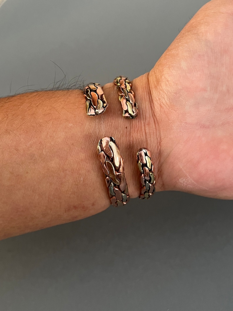 May include: Two copper bracelets with a textured, snake-like design. The bracelets are made of copper and have a gold and silver finish.