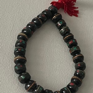 May include: A black beaded bracelet with red, green, and white accents. The bracelet has a red tassel.
