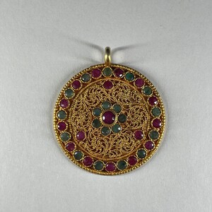 May include: A round gold pendant with a filigree design and a central ruby surrounded by smaller rubies and emeralds.