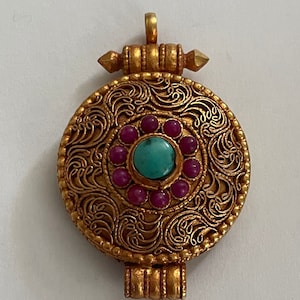 May include: A gold pendant with intricate floral designs and a turquoise stone surrounded by pink stones.