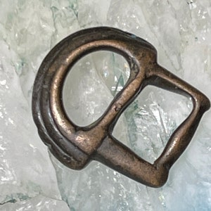 May include: A bronze-colored metal buckle with a D-shaped opening and a rectangular loop. The buckle is on a white background.