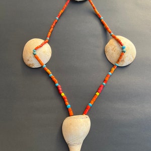 Könnte beinhalten: Eine Halskette aus orangefarbenen, roten und blauen Perlen hängt an drei weißen Muscheln. Die Halskette ist an einem weißen Muschel Anhänger mit einer spitzen Spitze befestigt.