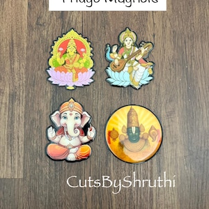 May include: Four colorful fridge magnets featuring Hindu deities. The magnets include images of Lakshmi, Saraswati, Ganesha, and Vishnu. The text "Fridge Magnets" is displayed at the top, and "CutsByShruthi" is at the bottom.