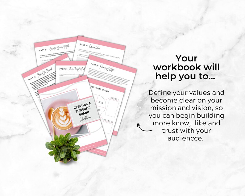 May include: A pink and white workbook with the title "Creating a Powerful Brand Workbook". The workbook is open to a page with a diagram titled "Personal Brand". A cup of coffee with latte art sits on a pink surface.
