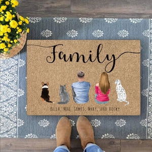 May include: A brown doormat with the word "Family" in black cursive lettering. There are four figures on the mat, two adults and two pets. The text below the figures reads "Bella, Max, James, Mary, and Rocky".