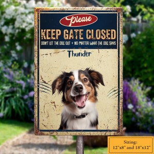 Op de afbeelding: Een vintage metalen bord met een blauwe achtergrond en witte tekst die "Houd de poort gesloten Laat de hond er niet uit X Het maakt niet uit wat de hond zegt." luidt. Het bord heeft een foto van een bruine, zwarte en witte hond met de naam "Thunder" onder de tekst. Het bord is verkrijgbaar in twee maten: 30,5 cm x 20,3 cm en 45,7 cm x 30,5 cm.