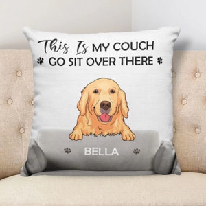 Może przedstawiać: Biała poduszka z golden retrieverem wystającym zza szarego poduszki kanapy. Poduszka ma napis "This is my couch go sit over there" z odciskami łap po obu stronach tekstu. Poduszka kanapy ma nadrukowane imię "Bella".