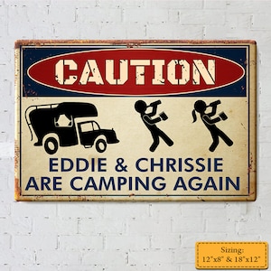 Könnte beinhalten: Ein Vintage-Schild aus Metall mit einem rot-weiß-blauen Warnschild. Das Schild lautet "ACHTUNG EDDIE & CHRISSIE SIND WIEDER CAMPING". Das Schild zeigt einen Comic-Campingbus, einen Mann und eine Frau, die aus Bechern trinken. Das Schild ist in zwei Größen erhältlich: 12"x8" und 18"x12".