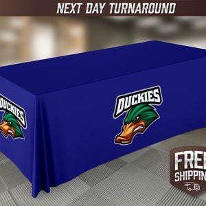 May include: A blue table cover with a green duck mascot logo that says "Duckies".