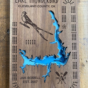 Pu&ograve; includere: Un cartello di legno con una mappa di un lago blu e un disegno di un uccello. Il cartello recita "LAKE THUNDERBIRD CLEVELAND COUNTY, OK J&K BODELL EST. 2007".