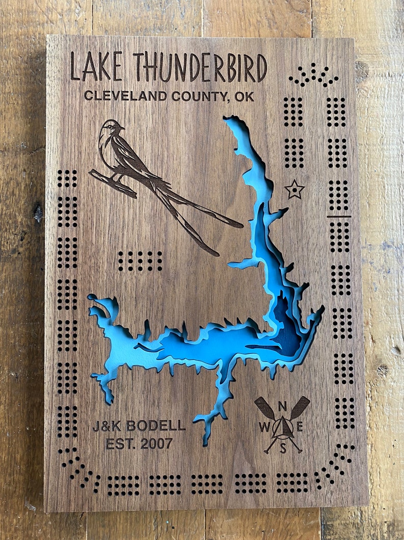 Pu&ograve; includere: Un cartello di legno con una mappa di un lago blu e un disegno di un uccello. Il cartello recita "LAKE THUNDERBIRD CLEVELAND COUNTY, OK J&K BODELL EST. 2007".