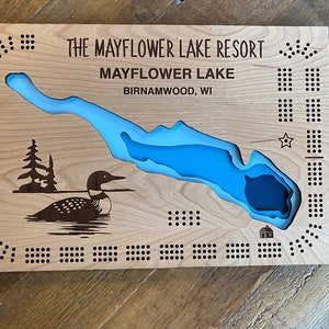 Pu&ograve; includere: Un tabellone da gioco in legno con un'incisione a forma di lago blu e un'illustrazione di un loon. Il tabellone &egrave; intitolato "The Mayflower Lake Resort" e "Mayflower Lake, Birnamwood, WI".