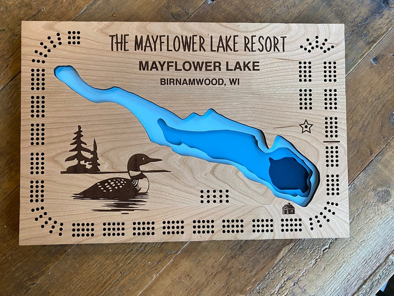 Pu&ograve; includere: Un tabellone da gioco in legno con un'incisione a forma di lago blu e un'illustrazione di un loon. Il tabellone &egrave; intitolato "The Mayflower Lake Resort" e "Mayflower Lake, Birnamwood, WI".