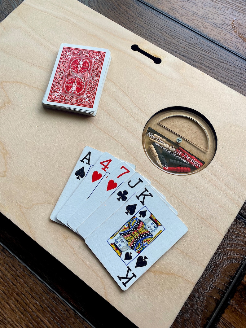 Pu&ograve; includere: Un tagliere di legno con un foro rotondo al centro. Il foro contiene un piccolo disco di legno con la scritta "Norffle Style Design" stampata su di esso. Ci sono cinque carte da gioco sul tagliere, tra cui un Asso di Picche, un 4 di Cuori, un 7 di Fiori, un Jack di Picche e un Re di Cuori. C'&egrave; anche un mazzo di carte nell'angolo in alto a sinistra del tagliere.