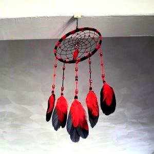 May include: A circular dream catcher featuring a black and red wrapped hoop with a black webbed center. Five hanging strands are decorated with red and black beads and finished with vibrant red and black feathers, creating a layered effect.