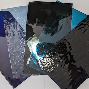 May include: Five different sheets of glass with a rippled texture. The glass sheets are in shades of blue, black, and gray.