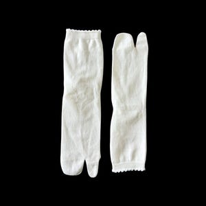 May include: A pair of white tabi socks with a split toe design. The socks have a delicate lace trim at the top.