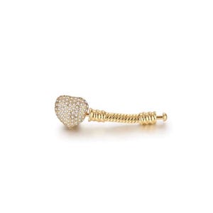 May include: A gold-colored charm with a heart-shaped design encrusted with small, clear crystals. The charm has a twisted, rope-like handle and a small, round end. The charm is designed to be used with a bracelet or necklace.