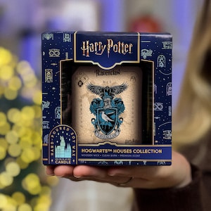 May include: A Harry Potter Ravenclaw candle in a decorative box. The box is navy blue with white and gold accents and the words "Harry Potter" at the top. The candle has a Ravenclaw crest and the words "Learning" and "Wisdom".