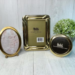May include: Three brass picture frames in different shapes. An oval frame with small feet, a rectangular frame, and a round frame. The rectangular frame has the text "Solid Brass" on the back.