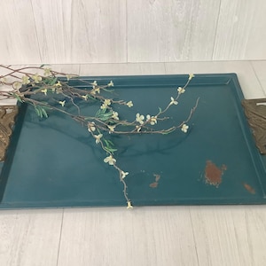 May include: Teal rectangular tray with ornate bronze handles. The tray has a distressed finish with some rust spots. A branch with small white flowers and green leaves is placed on the tray.