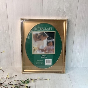 May include: A gold-colored photo frame with an oval green mat. The frame holds a picture of two people. The frame is 8x10 inches (20x25 cm) and is labeled "Intercraft".