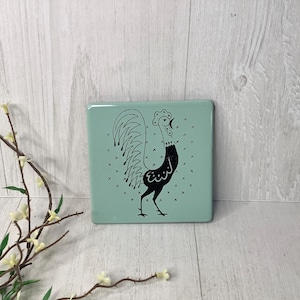 May include: A white ceramic mug with a black handle and the text "But First, Coffee" in a black, handwritten-style font. The mug is on a white surface.