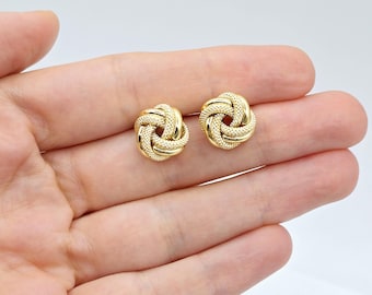 May include: A pair of gold knot-shaped earrings. The earrings are small and delicate, and they have a textured surface.