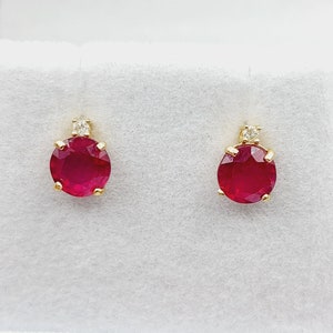 May include: A pair of ruby and diamond stud earrings. The earrings are set in gold and feature a round ruby gemstone with a smaller diamond accent.