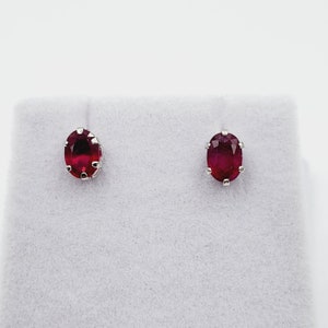 May include: A pair of silver stud earrings with oval-shaped red ruby gemstones.