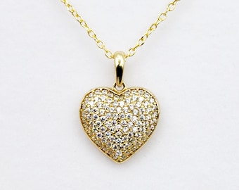 May include: A gold chain necklace with a heart-shaped pendant encrusted with small, clear cubic zirconia stones.