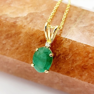 May include: A gold chain necklace with a pendant featuring a large oval emerald gemstone and a small diamond accent.