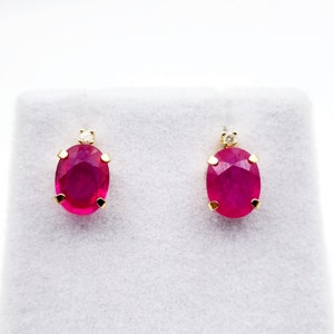 May include: A pair of oval ruby earrings with a single diamond accent on each earring. The earrings are set in gold.
