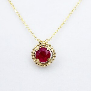 May include: A gold necklace with a red ruby pendant set in a gold bezel with a beaded edge.